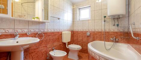 Un baño con lavamanos, bidé, inodoro y bañera, todos con accesorios blancos y suelo de baldosas.