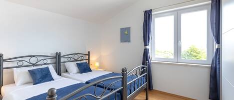 Een slaapkamer met twee bedden, een raam met gordijnen, een bedlampje en een klein schilderij aan de muur.