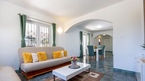 A modern living room with a sofa, a coffee table with a vase of flowers, and a dining area with chairs and a table. - Apartments Maja (Rogoznica)