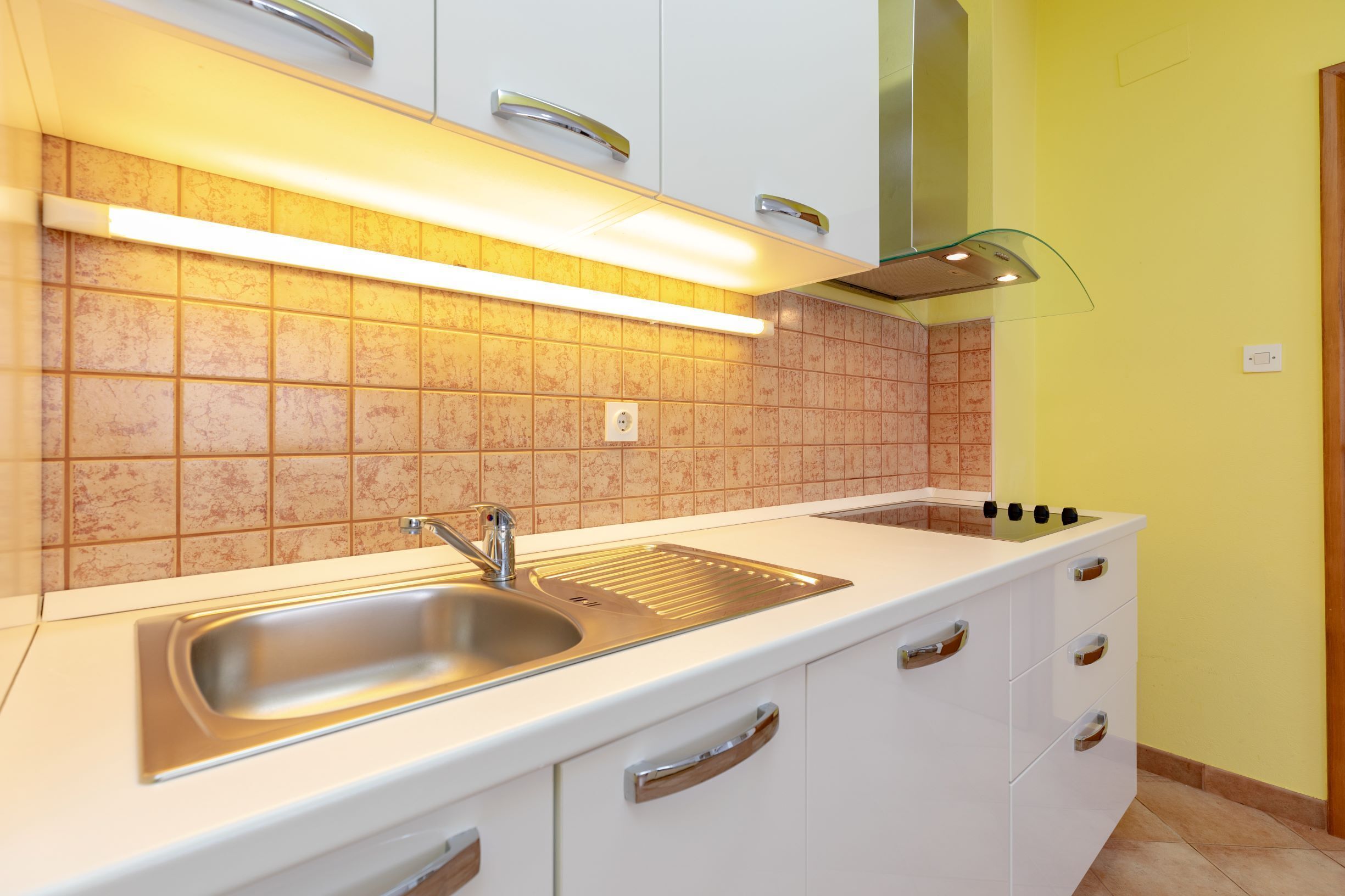 Une cuisine moderne avec des meubles blancs, un évier en acier inoxydable et un dosseret carrelé.