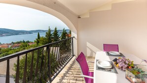 A balcony with a table set for two, overlooking a lake and hills. - Apartments Maja (Rogoznica)