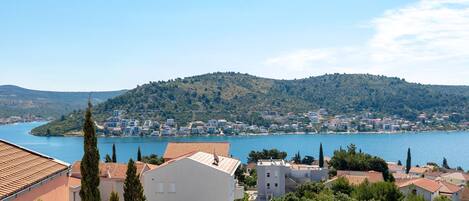 En kystby med bygninger tæt ved vandet, en bakke i baggrunden og en klar himmel.