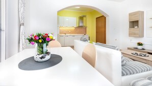 A modern living room with a dining table, a sofa, and a kitchen in the background. - Apartments Maja (Rogoznica)