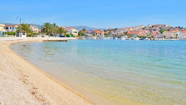 A coastal town with a sandy beach, clear blue water, and buildings in the background. - Apartments Maja (Rogoznica)