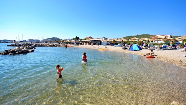 A beach scene with clear water, people swimming, and beach umbrellas. - Apartments Smilja (Tribunj)