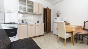 A compact kitchen with a stove, cabinets, and a dining area with a table and chairs. - Apartments Smilja (Tribunj)