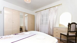 A bedroom with a bed, a wooden wardrobe, a chair, a vanity with a mirror, and a window with curtains. - Apartments Smilja (Tribunj)