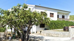 A white building with a balcony, a tree in front, and a stone wall. - Apartments Smilja (Tribunj)