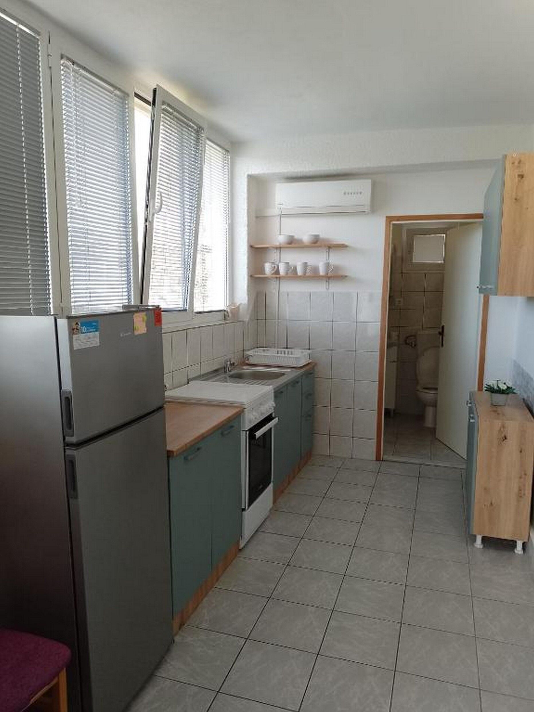 A compact kitchen with a refrigerator, stove, and sink. There are shelves above the counter and a small cabinet to the right.
