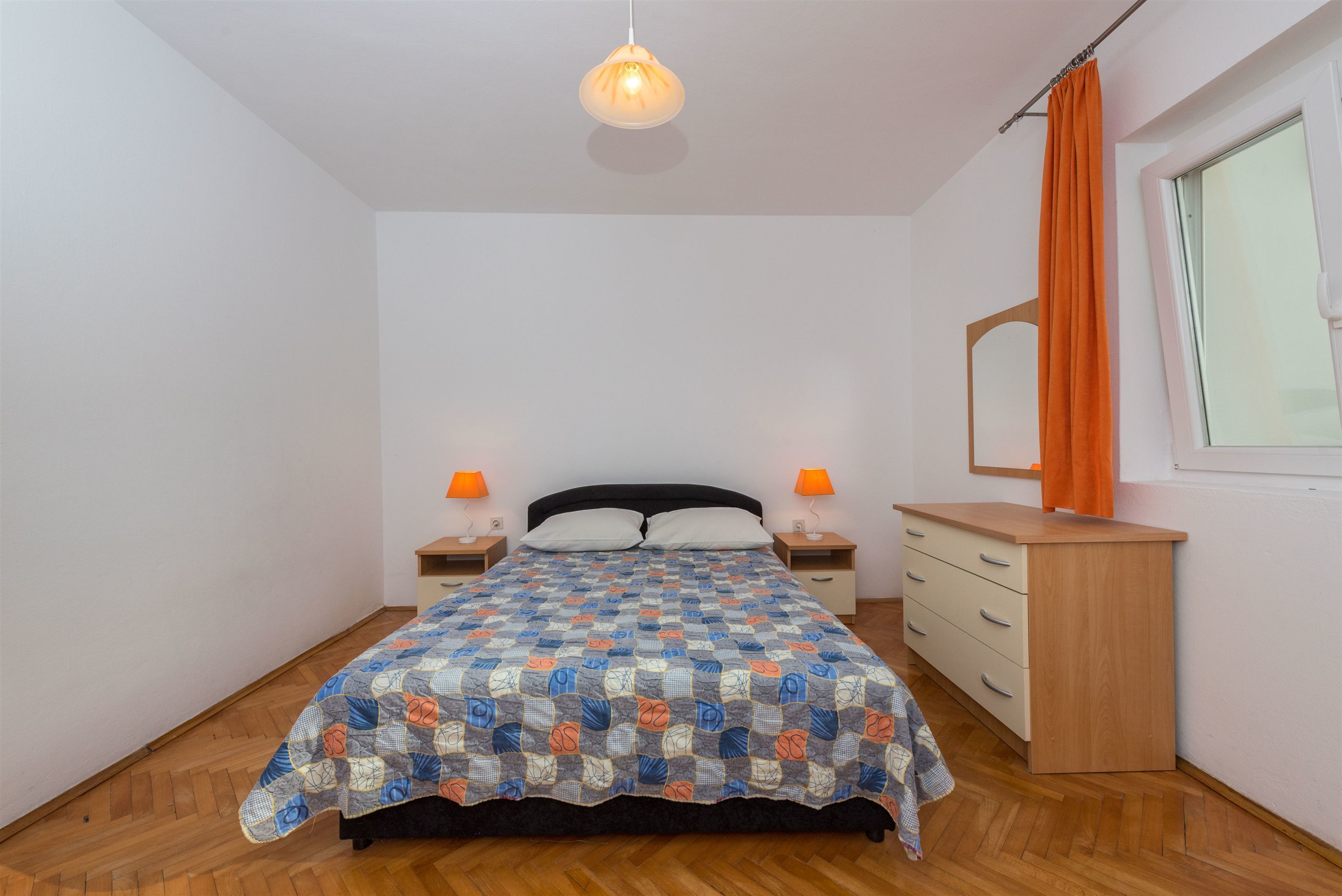 Ein Schlafzimmer mit einem Bett, zwei Nachttischen, einer Kommode und einem Fenster mit Vorhängen.
