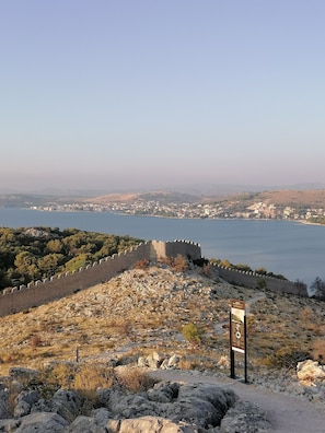 Un site historique doté d’un mur de pierre et d’un panneau d’information, qui offre une vue sur une ville côtière et une étendue d’eau.