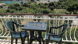 Een balkon met twee stoelen en een tafel, met uitzicht op een schilderachtig glooiend landschap met gebouwen en een waterpartij.