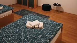 Een slaapkamer met twee bedden, een kledingkast, een klein rond tafeltje en een raam met jaloezieën.
