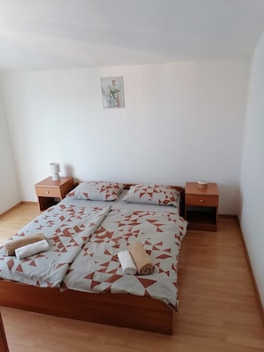En snyggt bäddad säng med geometriskt mönstrade sängkläder, två sängbord i trä med lampor och en enda inramad tavla på väggen.