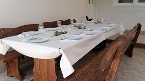 Een eettafel gedekt voor zes personen, met witte tafelkleden, houten banken en een schilderij aan de muur.