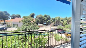 A balcony with a view of a street, trees, and a building with a red roof.