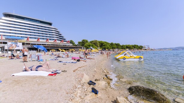 A beach with people sunbathing, umbrellas, and a boat.