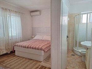 A bedroom with a bed, a bedside table, a lamp, and a window with sheer curtains.