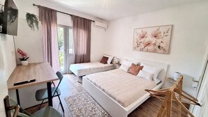 A bedroom with two beds, a desk, a chair, a hanging plant, and a window with curtains.