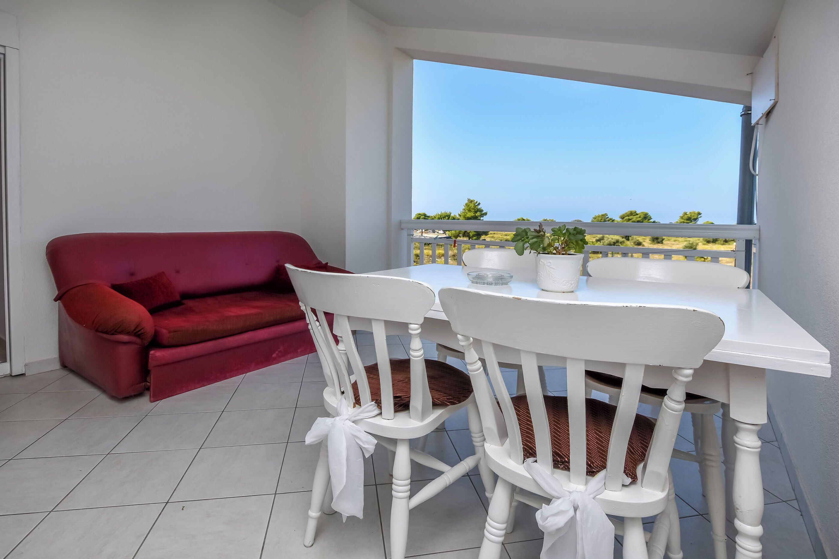 A balcony with a white table and chairs, a red sofa, and a view of the sea.