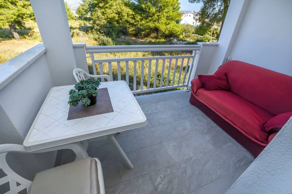 A balcony with a white table, a red sofa, and a potted plant.