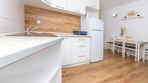 Una cocina moderna con armarios blancos, protector contra salpicaduras de madera, horno empotrado y una zona de comedor con mesa y sillas blancas.
