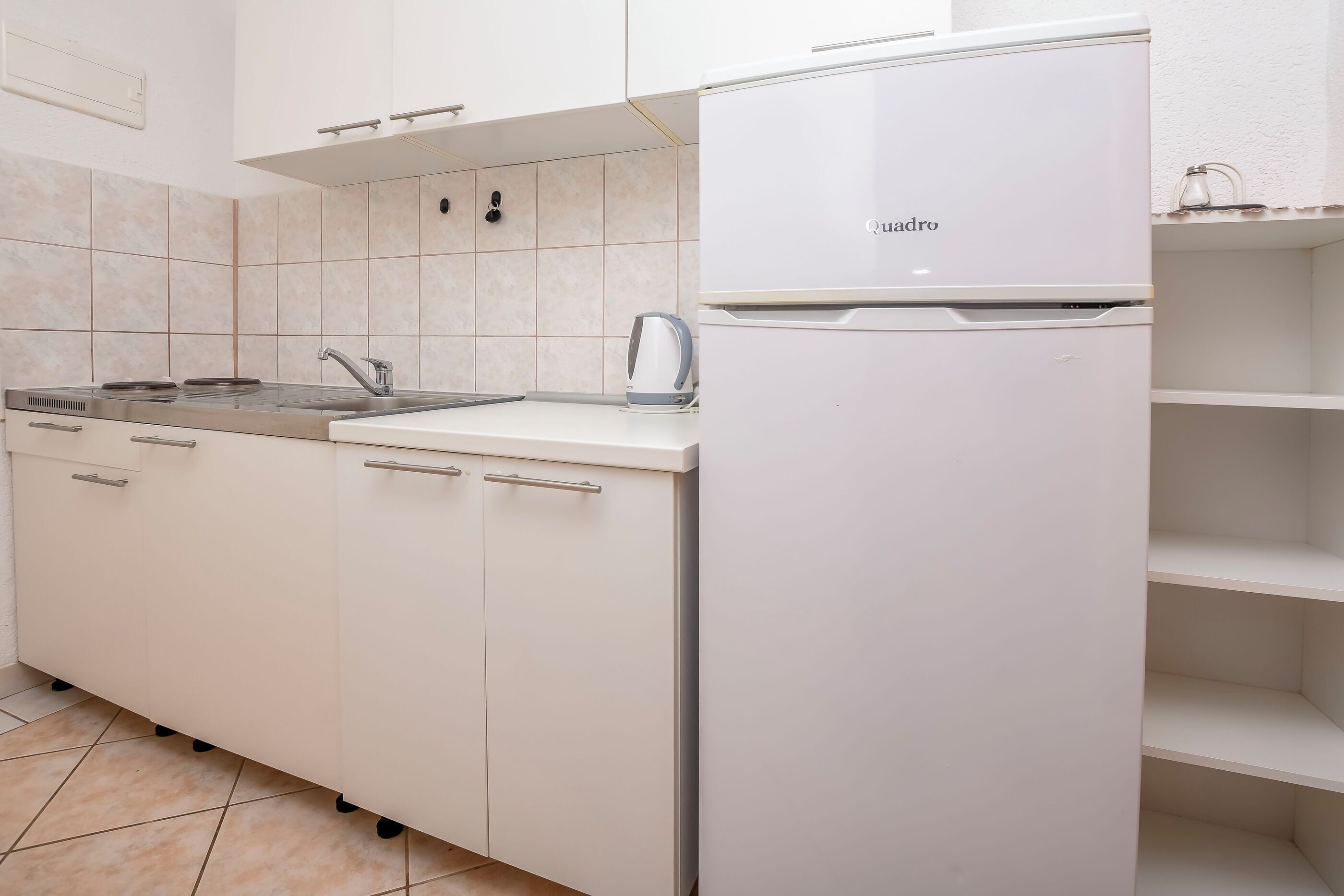 Een keuken met witte kasten, een fornuis, een spoelbak en een koelkast.