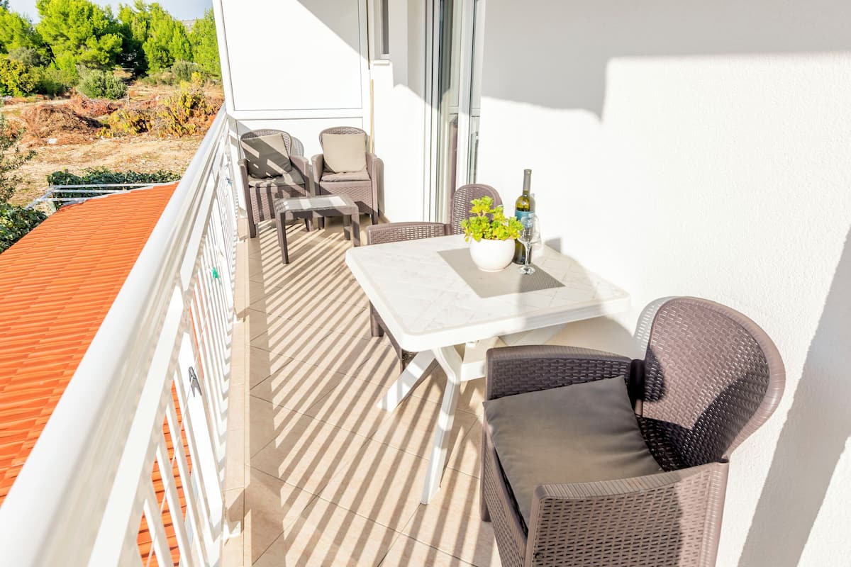 A balcony with wicker furniture, a table with a vase of flowers, and a bottle of wine.