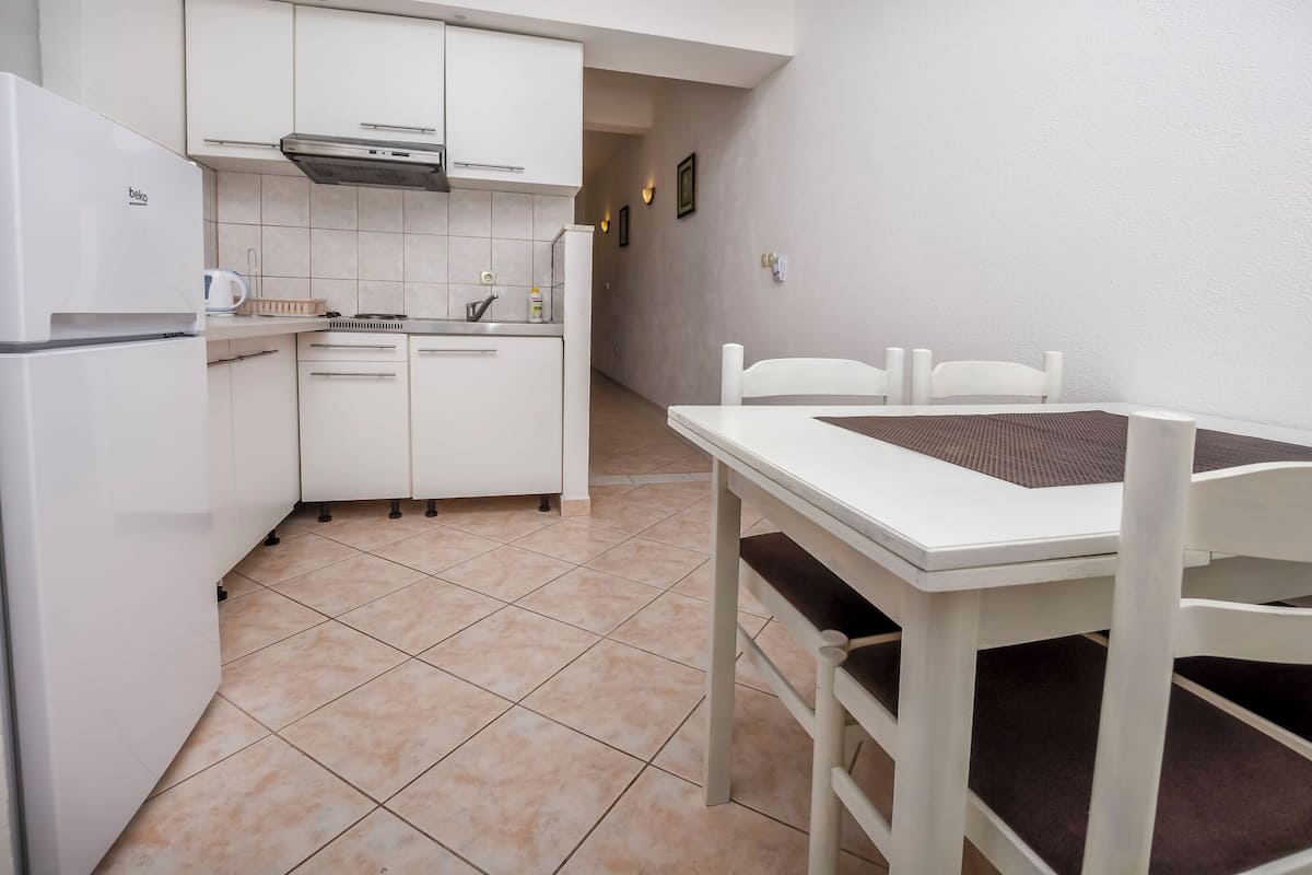 A compact kitchen with white cabinets, a built-in oven, and a small dining area with a white table and chairs.