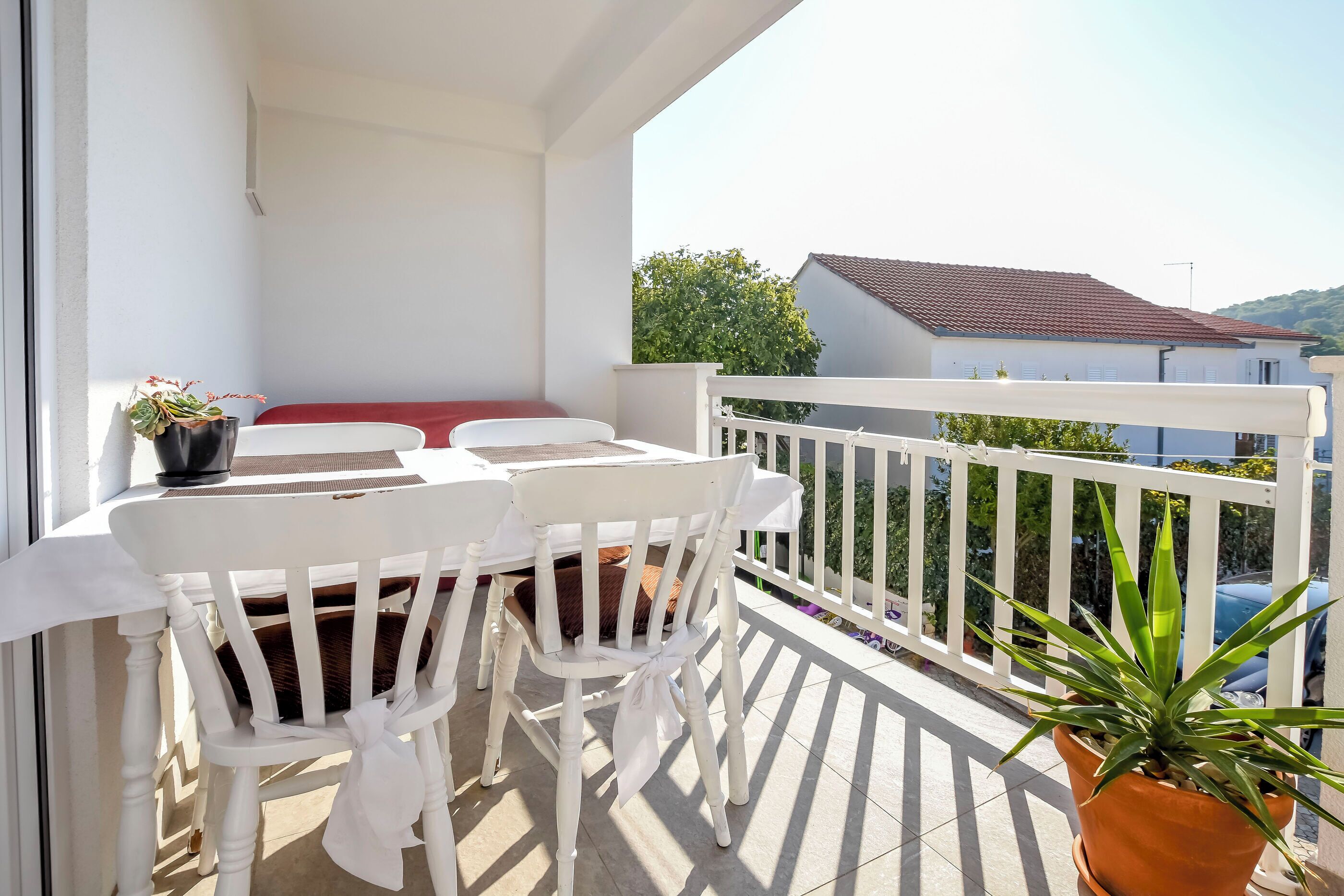 A balcony with a white table and chairs, a red cushion, and a potted plant.
