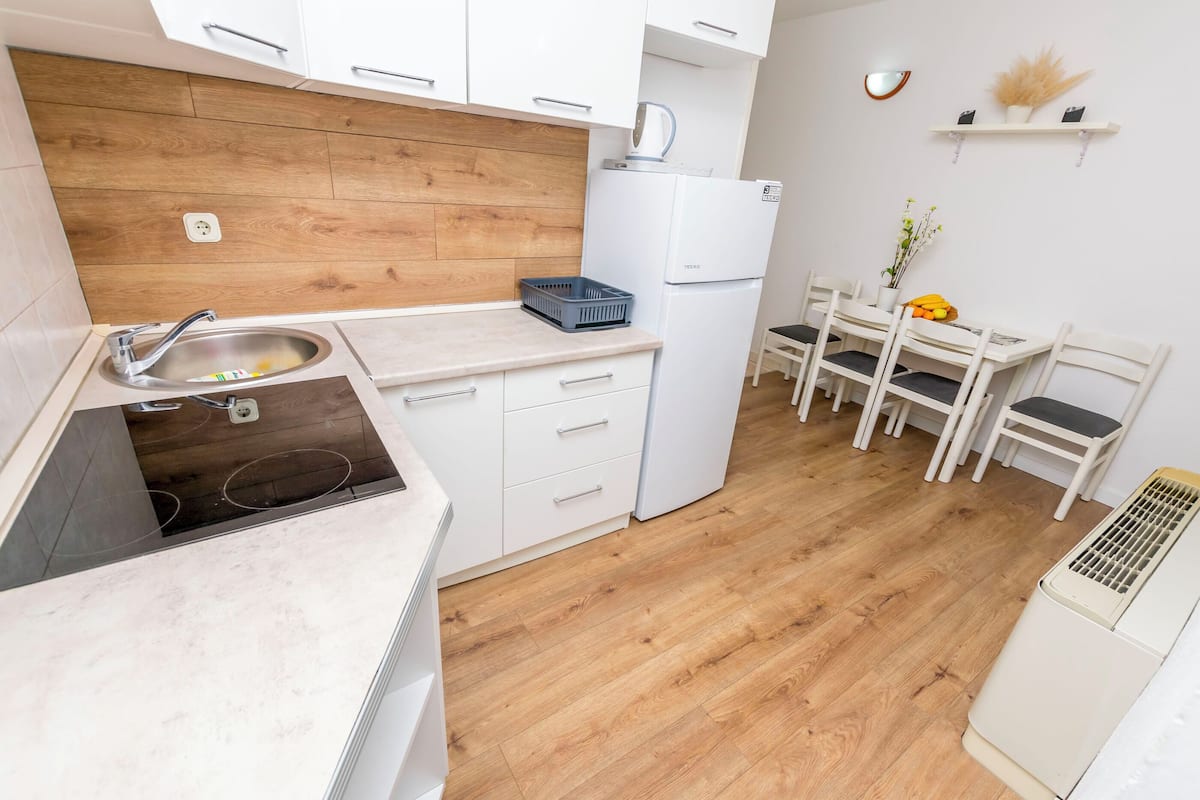 A modern kitchen with white cabinets, a wooden backsplash, a built-in dishwasher, and a dining area with a white table and chairs.