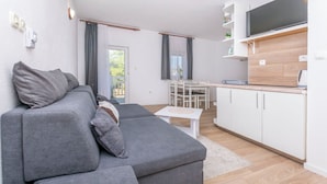 Una sala de estar moderna con un sofá seccional gris, una pequeña mesa blanca y una cocina con armarios blancos y encimera de madera.