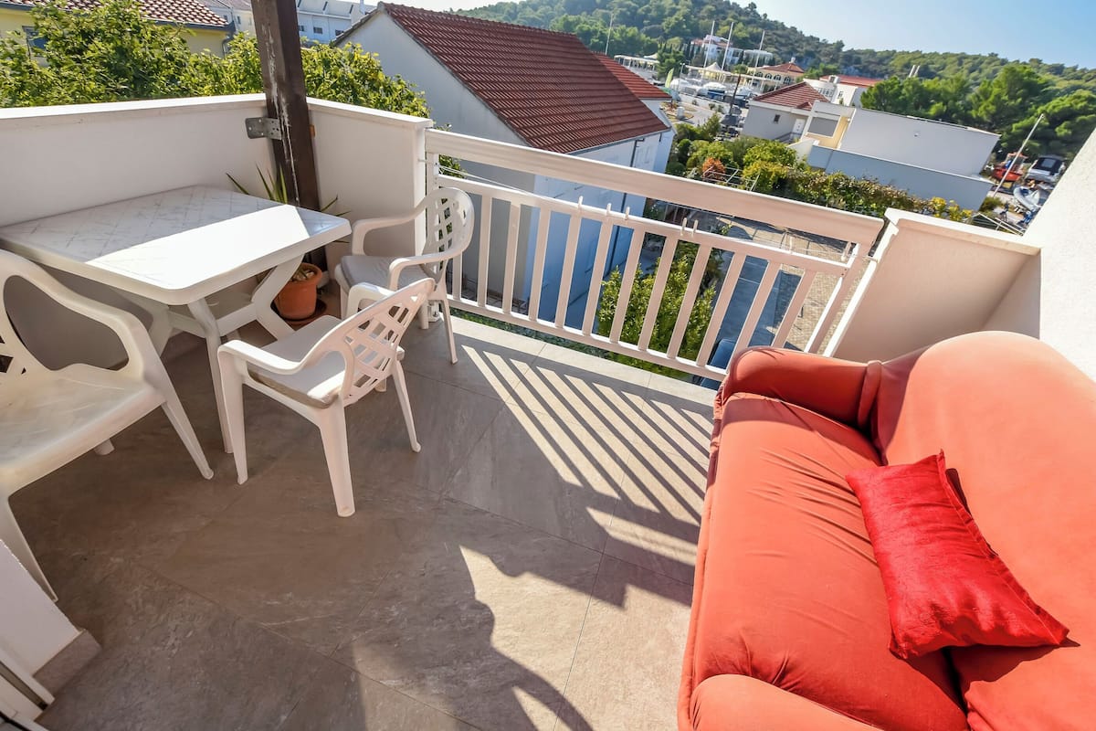A balcony with a white table and chairs, a red sofa, and a view of buildings and greenery.