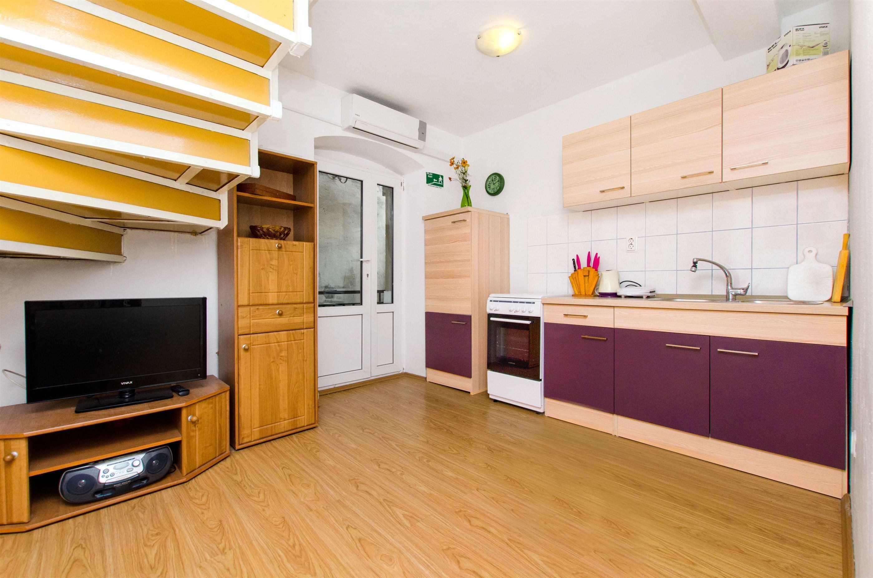 A modern kitchen with wooden cabinets, a built-in oven, and a flat-screen TV.