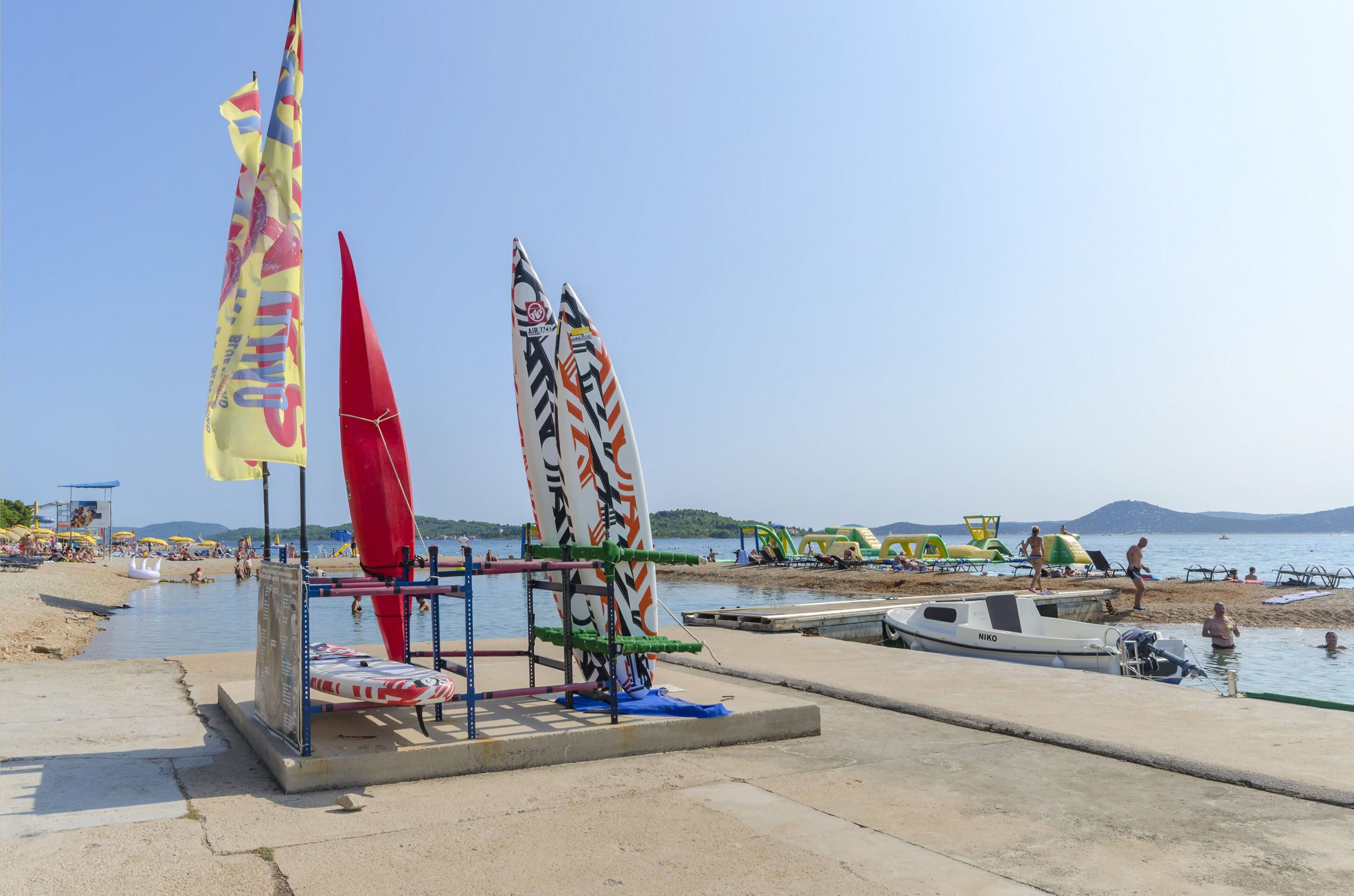 Una zona sulla spiaggia con un molo per barche, un rastrelliera per tavole da surf e sedie da spiaggia.