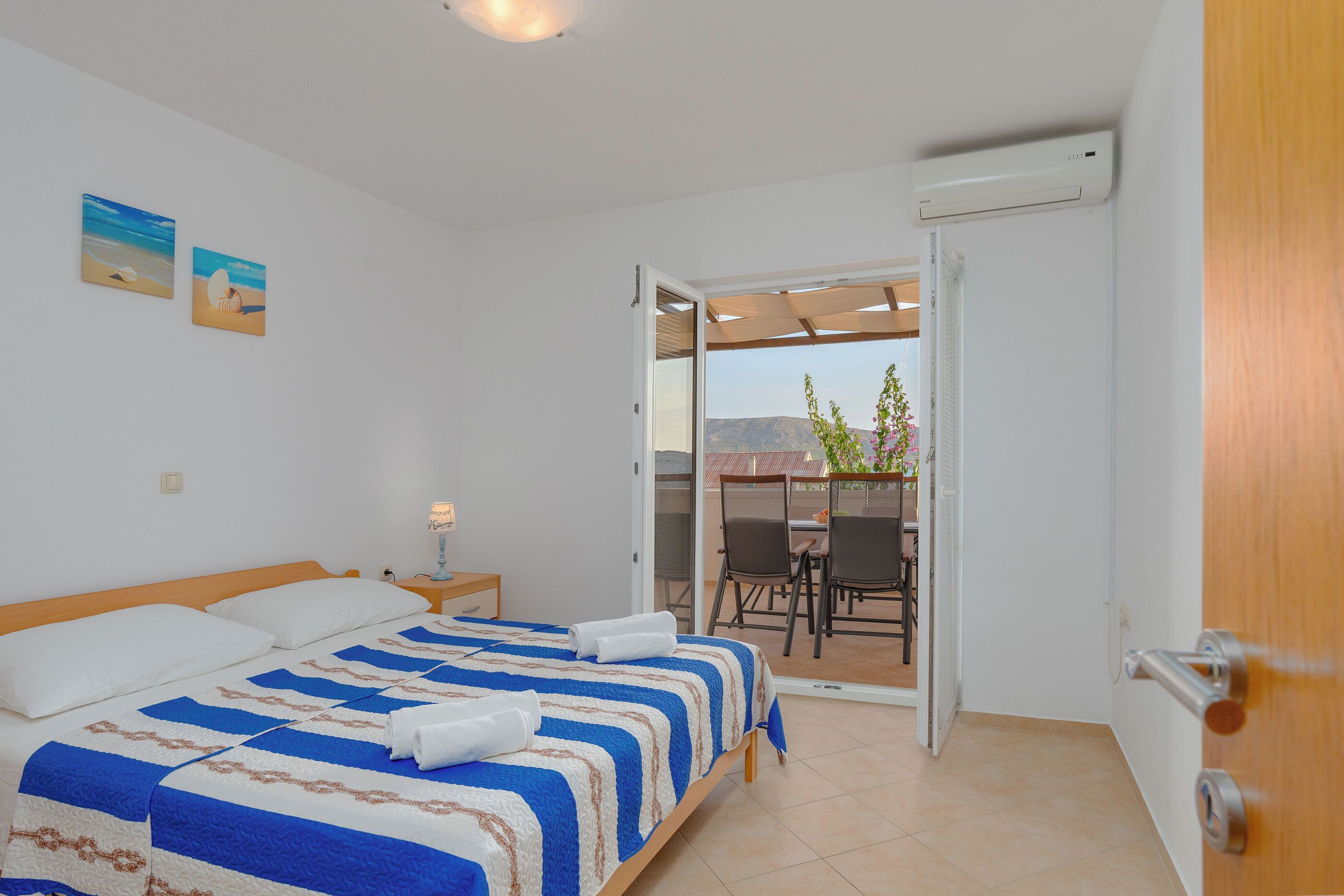 A bedroom with a bed, a nightstand, and a view of a balcony with chairs and a table.