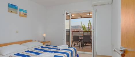 A bedroom with a bed, a nightstand, and a view of a balcony with chairs and a table.