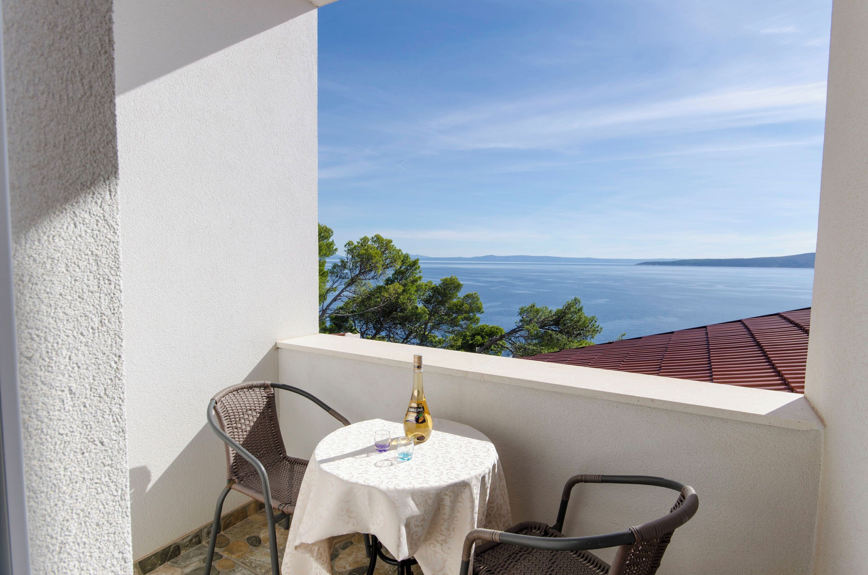 Uma varanda com mesa e cadeiras, com vista para o mar e árvores.