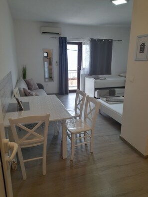 A modern, well-lit room with a dining table, chairs, a sofa, a bed, and a balcony with curtains. - Apartments Stipe (Omis)