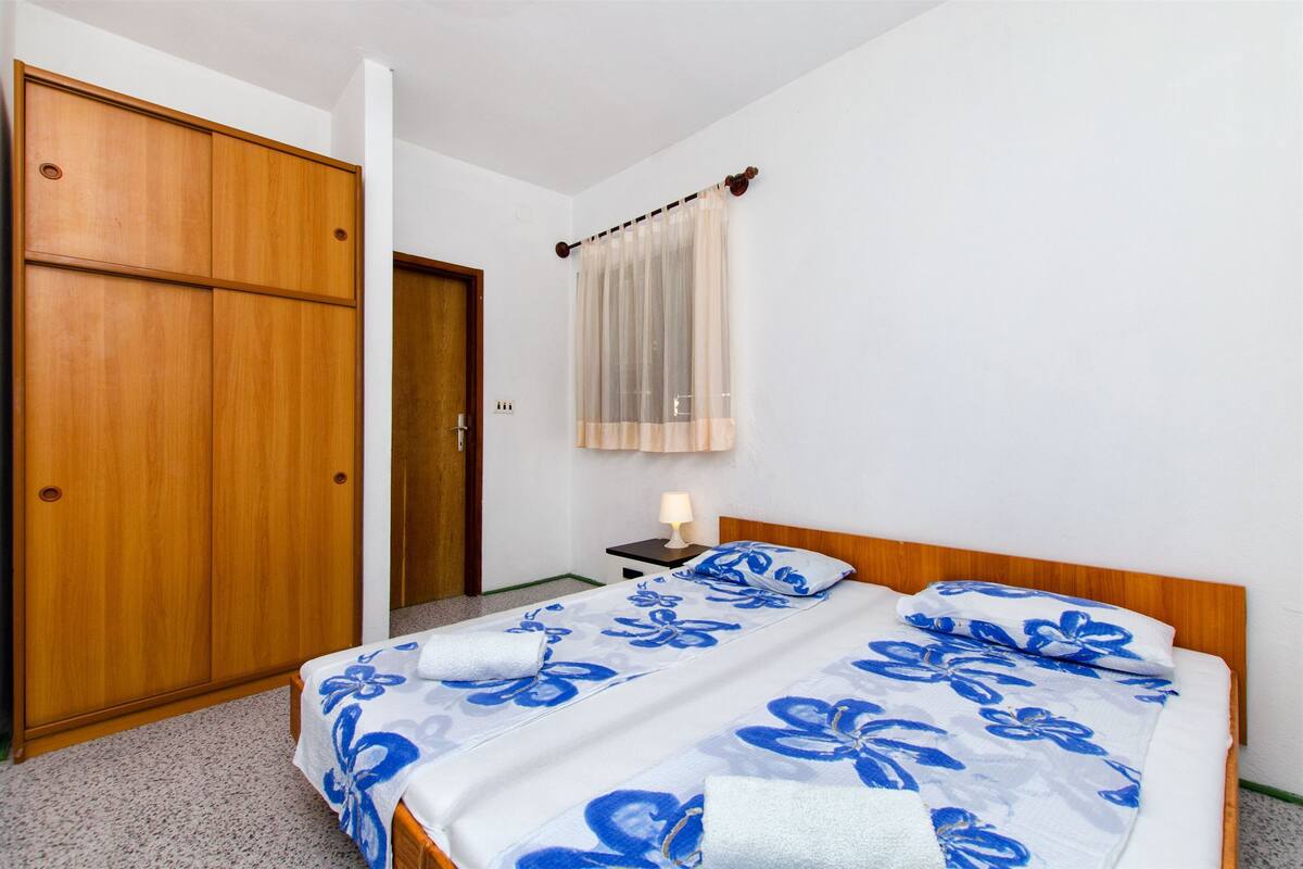 A bedroom with a double bed, wooden wardrobe, and a bedside table with a lamp.