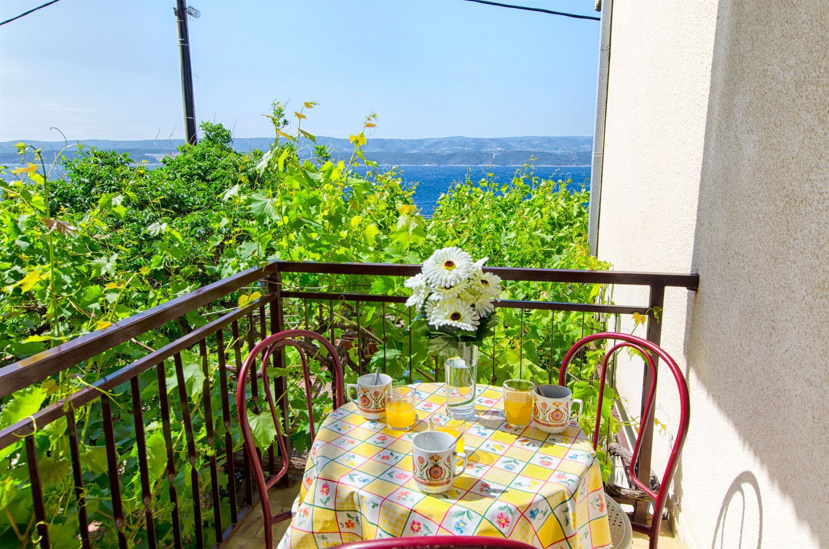 Uma varanda com uma mesa posta para dois, um vaso de flores e vista para o mar.