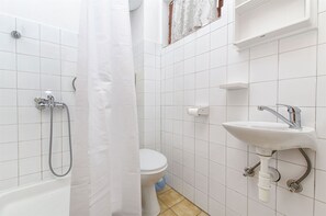 Een badkamer met witte tegels, een badkuip, een toilet en een wastafel.