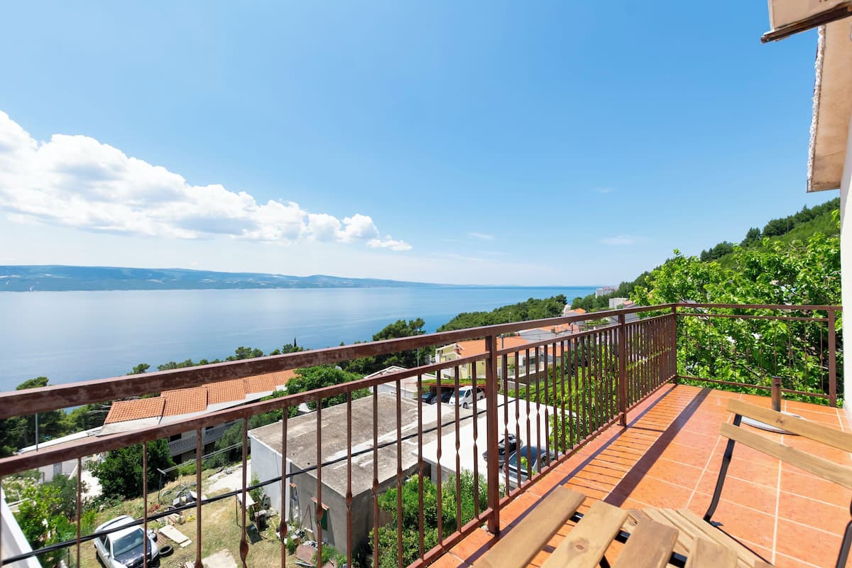 A balcony with a metal railing overlooking a body of water and a distant shoreline.