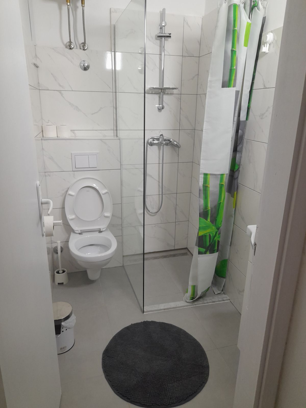 Ein modernes Badezimmer mit Duschkabine aus Glas, Toilette und schwarzem Teppich auf dem Boden.