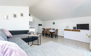 Een moderne woonkamer met een bank, eettafel, stoelen, een televisie en een keukenhoek.