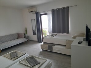 Een moderne kamer met een bank, een bed met televisie, een bureau en een balkon met gordijnen.