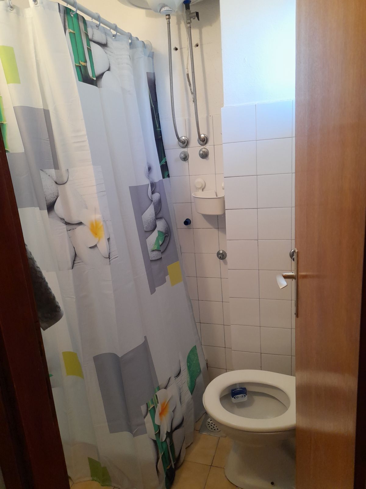 A bathroom with a shower, toilet, and a curtain with floral patterns.
