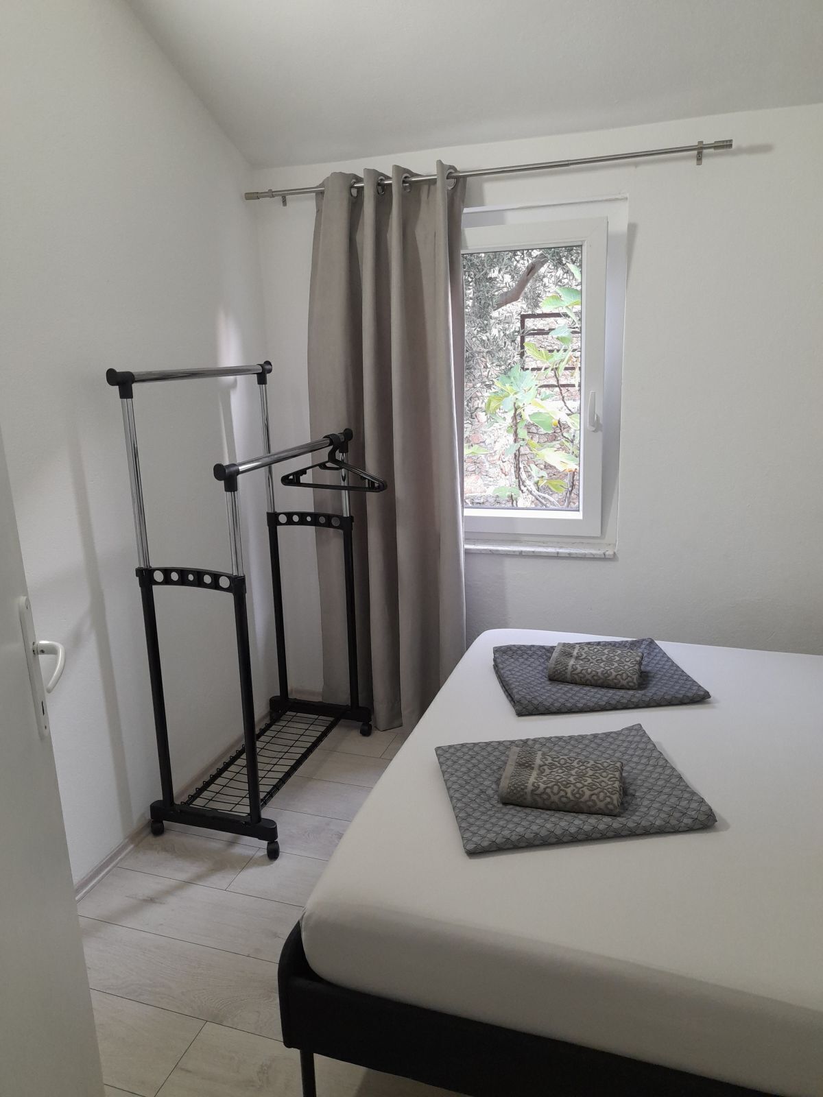 Une chambre à coucher avec un lit, une fenêtre avec des rideaux et un étendoir à linge en métal.