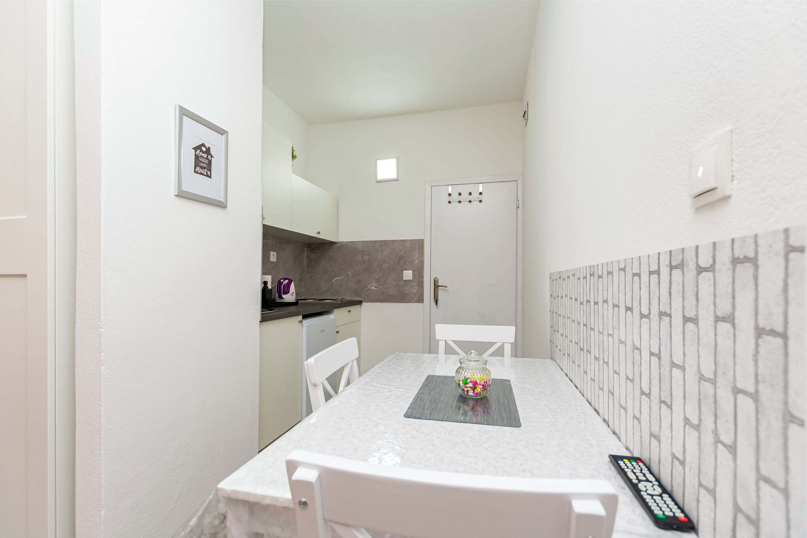 A compact kitchen with white cabinets, a marble countertop, and a small dining area with a table and chairs.