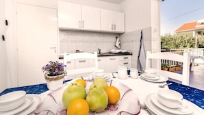 A modern kitchen with white cabinets, a blue countertop, and a dining area with white tableware and fresh fruits.